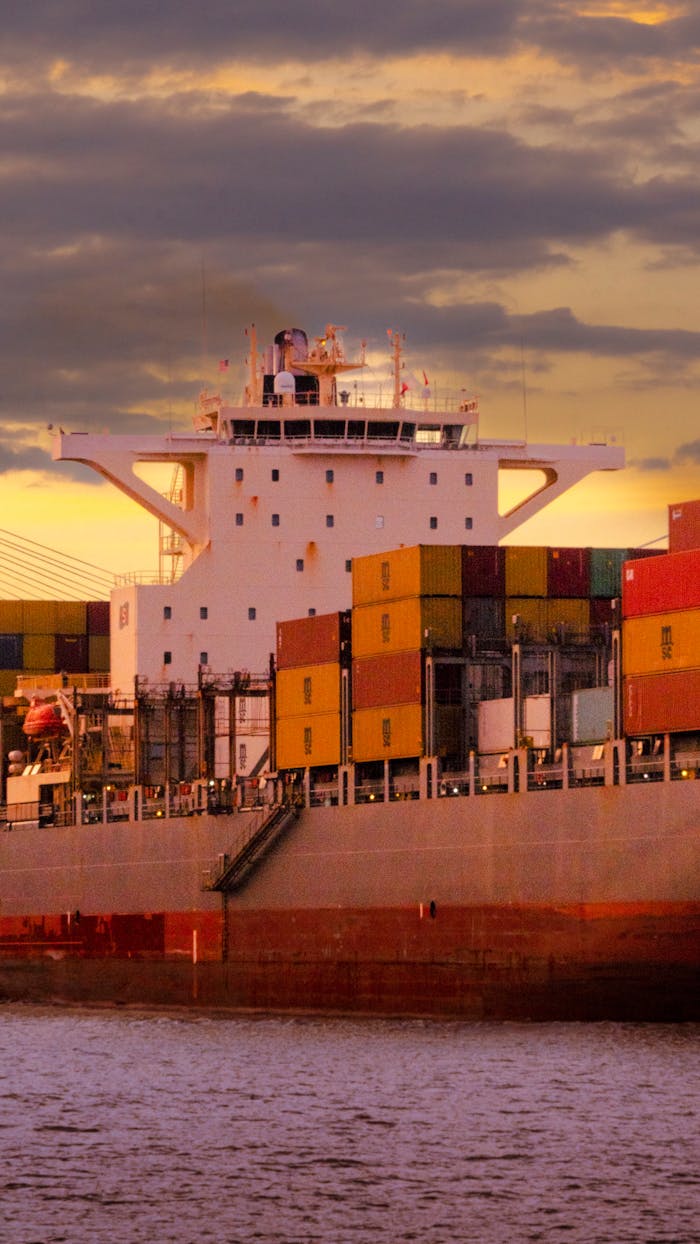 Cargo ship loaded with colorful containers against a vibrant sunset sky.