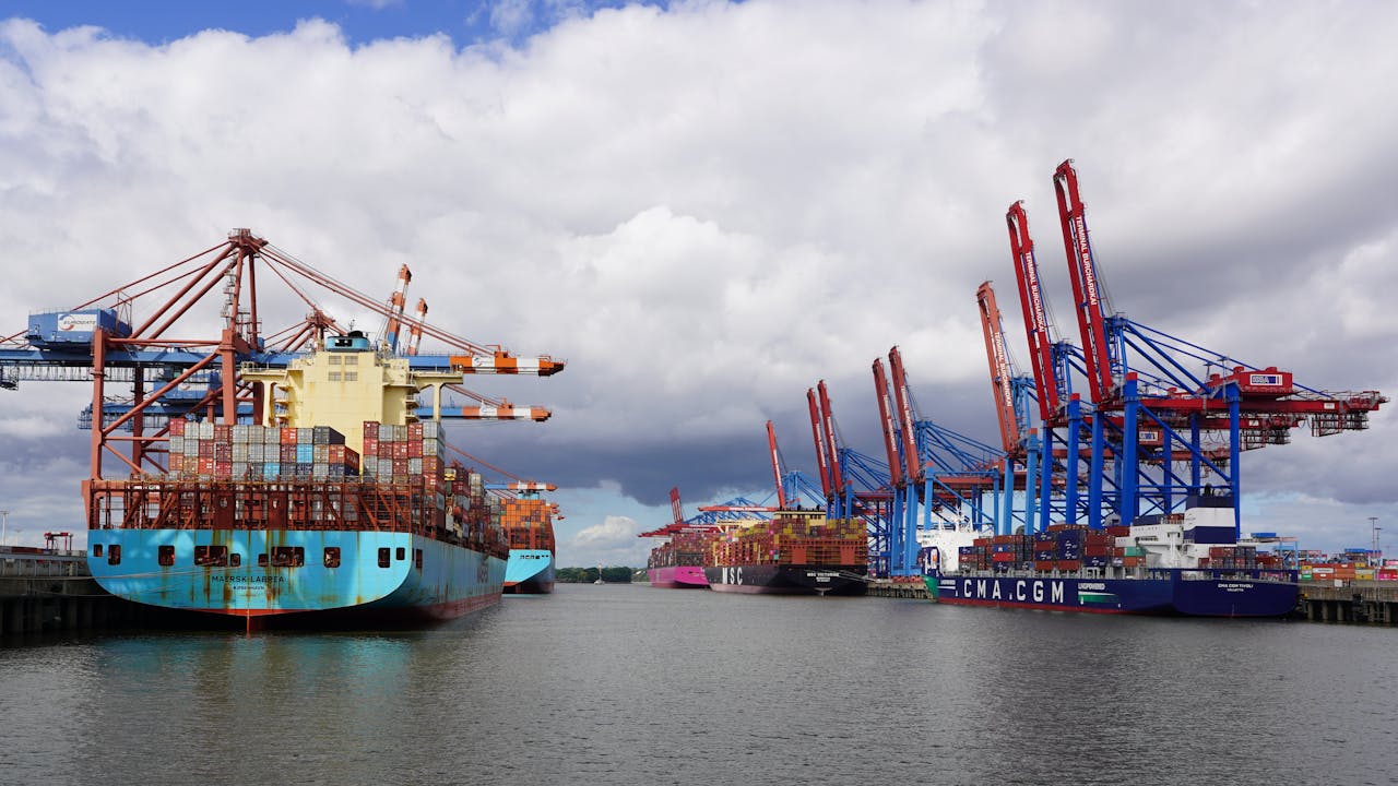 Wide-angle view of container ships docked at Hamburg port under cloudy skies, showcasing global trade.